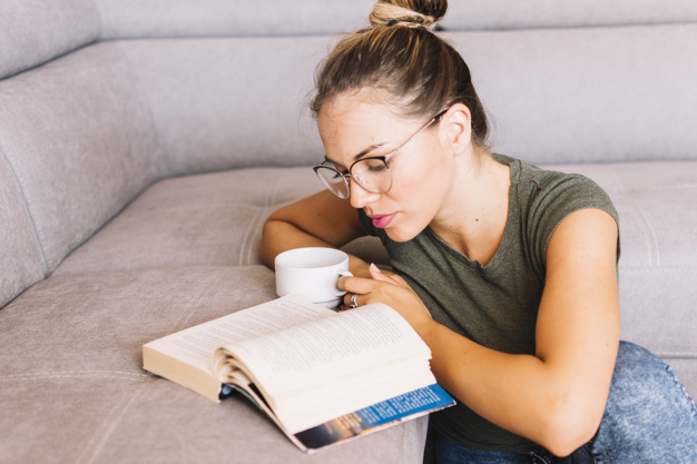 Young woman holding coffee cup reading book - Nohat
